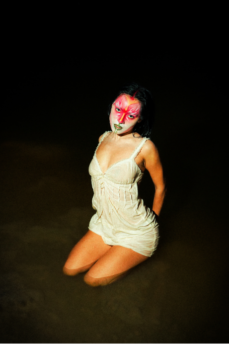 Model kneeling in a white slip dress with pink graphic face makeup